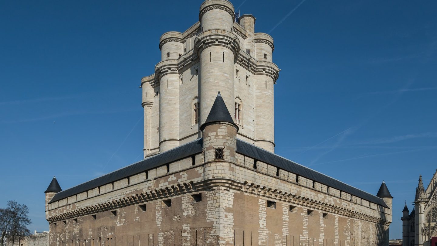 The keep of the Château de Vincennes photographed from the south-west, a tall square tower with four round corner turrets rising above a lower curtain wall and a dry ditch
