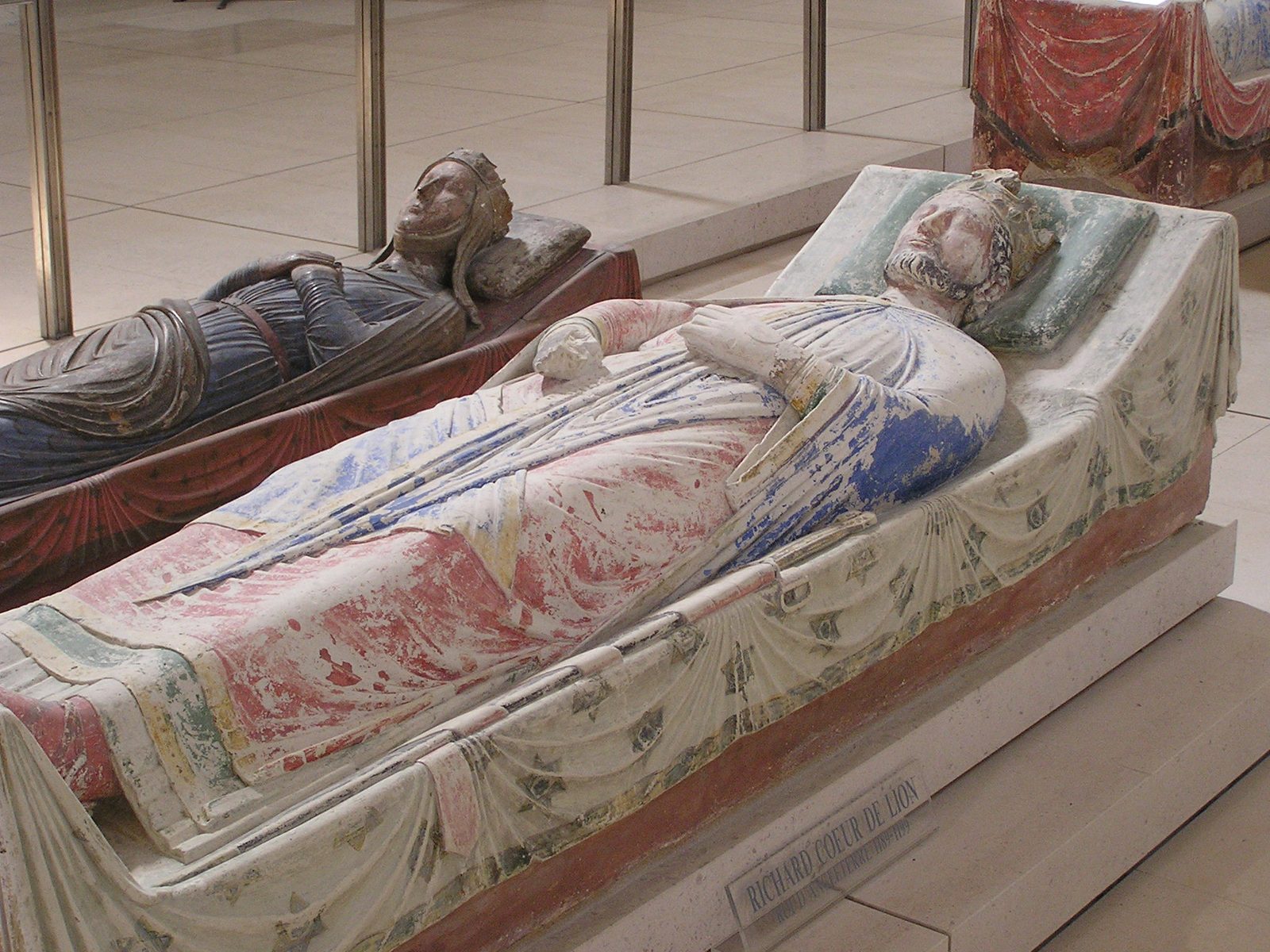 Photograph of Richard the Lionheart's painted stone tomb effigy at Fontevraud Abbey, showing the crowned king lying in repose with another painted effigy visible behind him